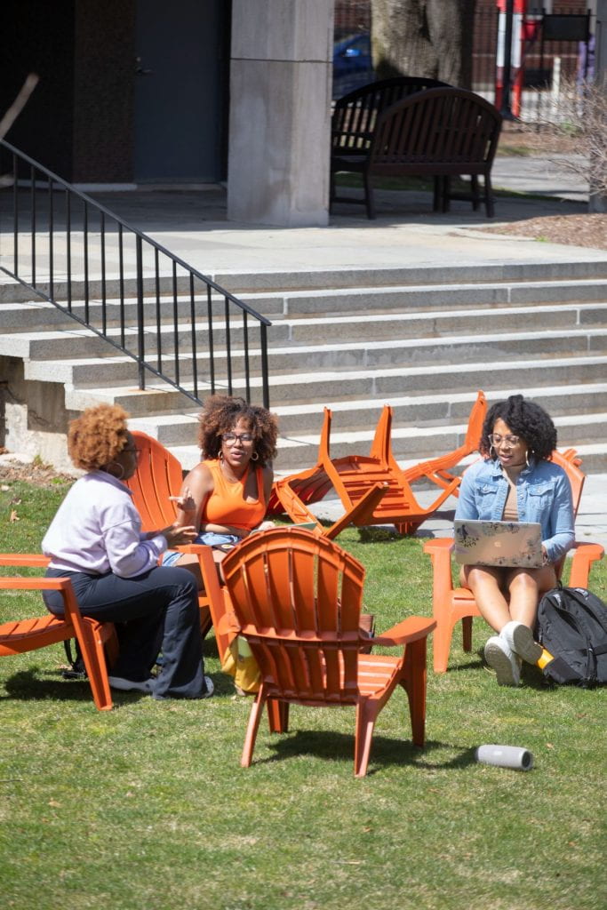 Three student sitting in the red colored chairs at Harvard yard